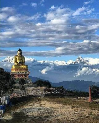 Golden Buddha statue in Pokhara, Nepal with stunning Himalayan mountain peaks and cloudy sky in the background.
